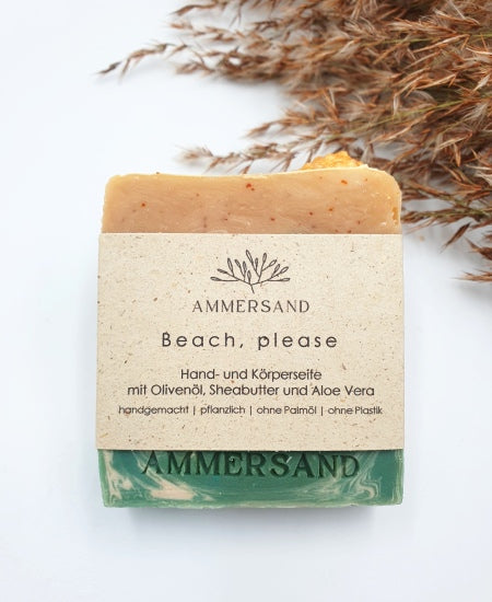 Handgemachtes rechteckiges Seifenstück in Meeres-Look mit weiß-blauen Wellenmuster und gelbem Sand mit goldener Muschel aus Seife mit Graspapier-Etikett
