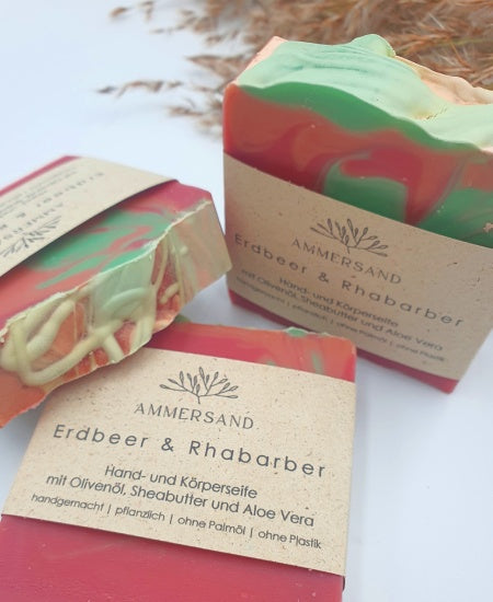 Drei handgemachte rote Seifenstücke mit Papierbanderole auf weißem Hintergrund mit Schilfgras Nahaufnahme