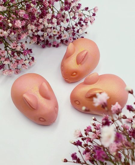 Rosafarbene Seifenstücke in süßer Häschenform mit goldenem Dekor auf weißem Hintergrund mit zarten Blüten