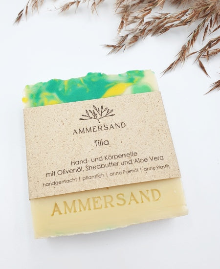 Beige Seifenstücke mit grünen und gelben Marmorierungen und Prägung "Ammersand" auf weißem Hintergrund mit Schilfgras