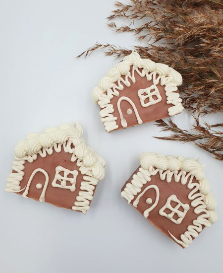 Handgemachte Seifenstücke in Form von Lebkuchenhäusern auf weißem Hintergrund mit Schilfgras